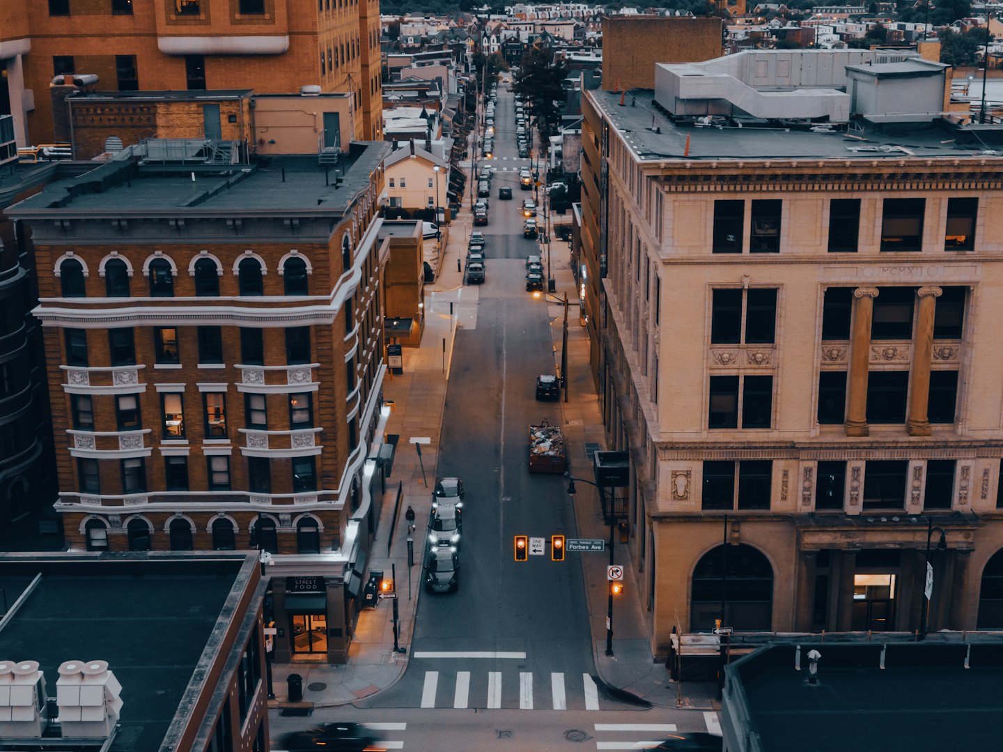 Luftaufnahme einer ruhigen Stadtstraße in der Dämmerung mit beleuchteten Straßenlaternen.
