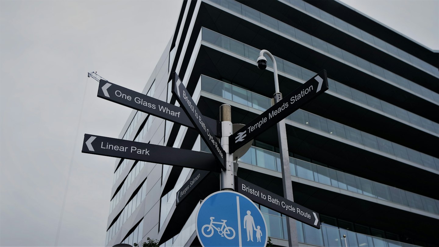 Ein mehrseitiger Wegweiser steht vor einem modernen Glasbürogebäude.