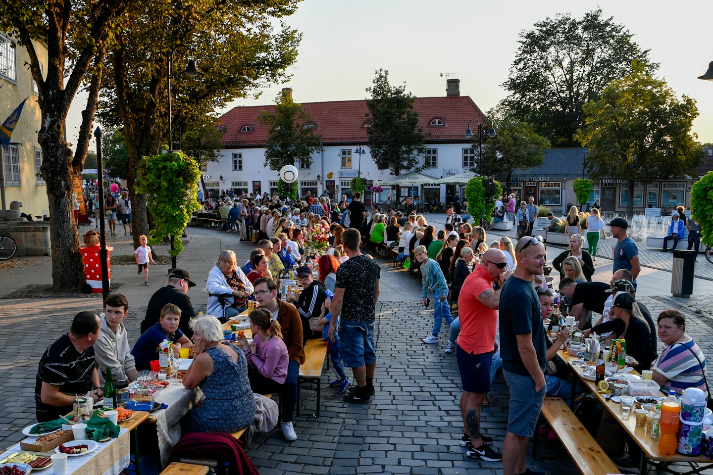 Menschen genießen Essen und Trinken an Tischen auf einem Stadtplatz in der Dämmerung.