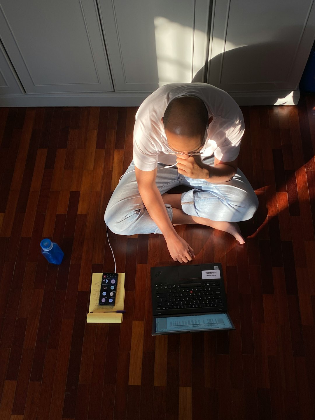Eine Person arbeitet im Schneidersitz auf einem Holzboden an ihrem Laptop.